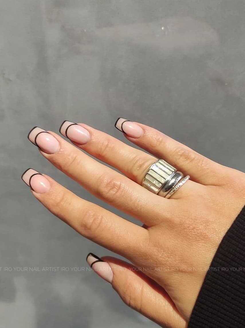 A hand with nude square nails with black French tip contours