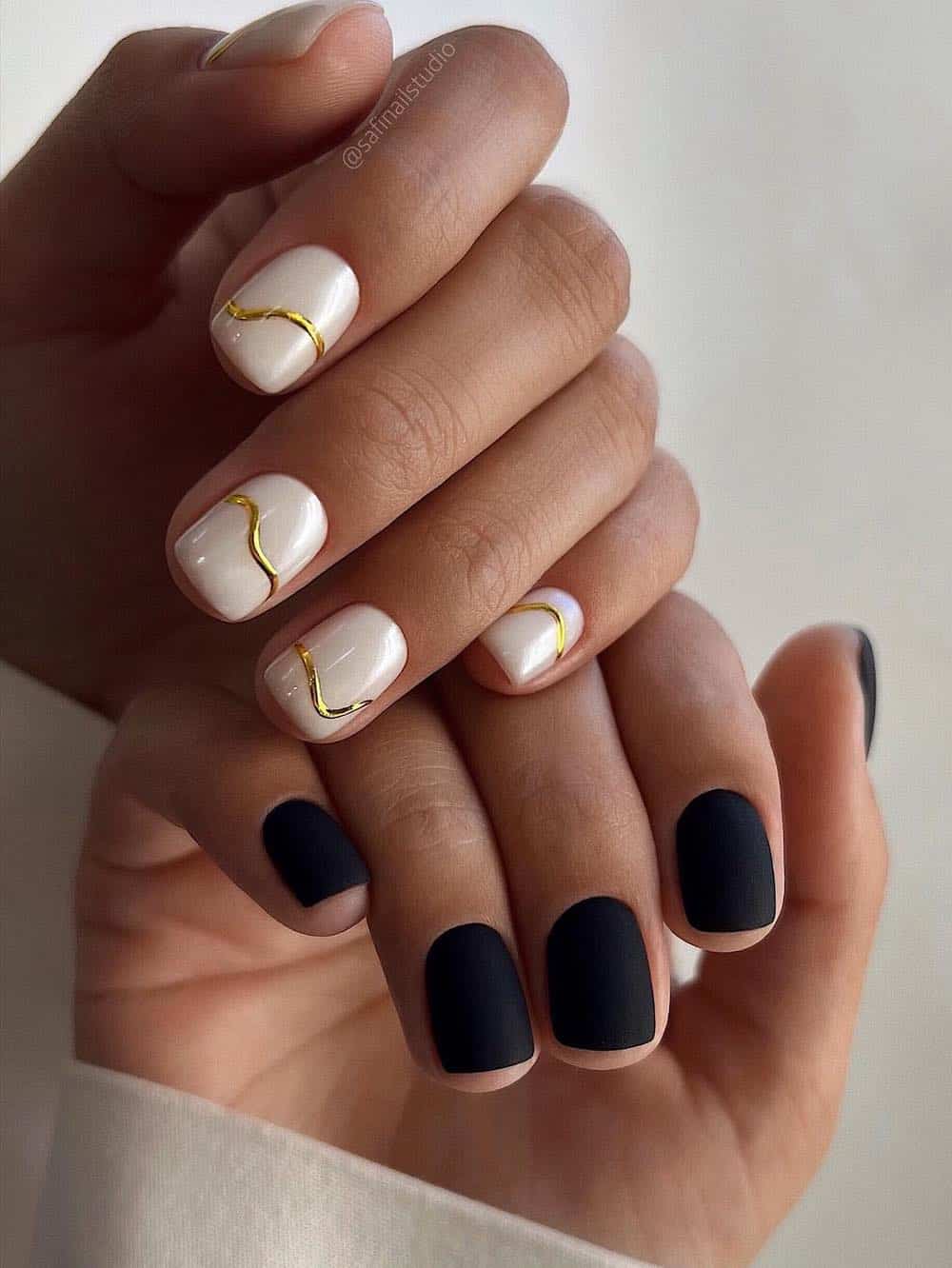A nail polish featuring a short, matte black polish on one side and a glossy white polish with crisp gold accents on the other