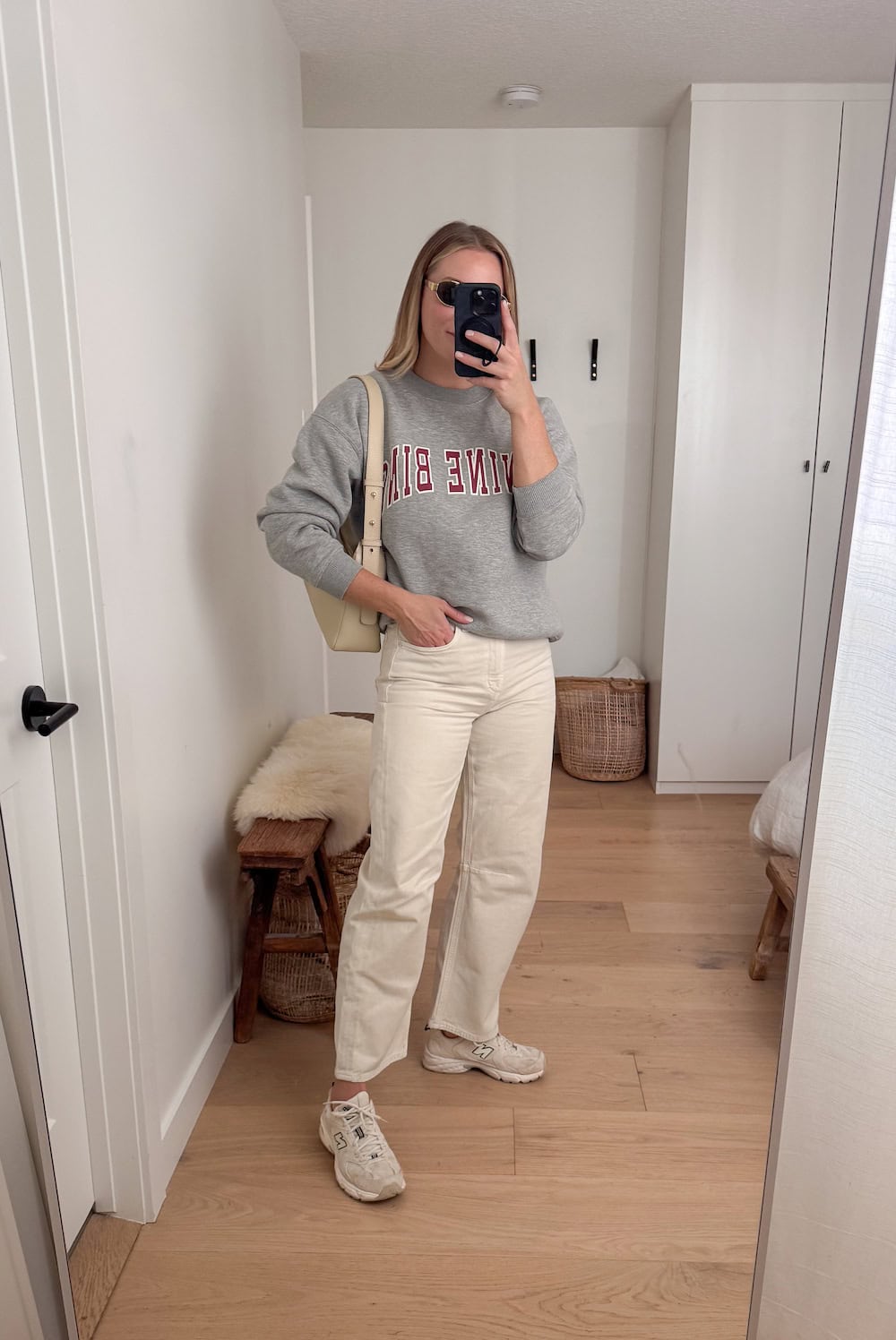 Christal wearing white jeans and a graphic crew neck sweatshirt with New Balance sneakers.