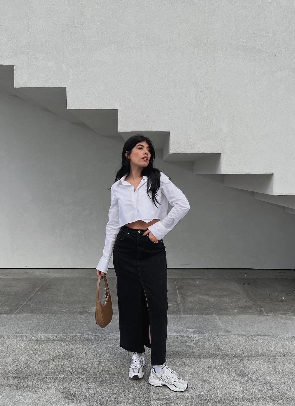 Woman wearing a black denim skirt with New Balance sneakers and a cropped button down.