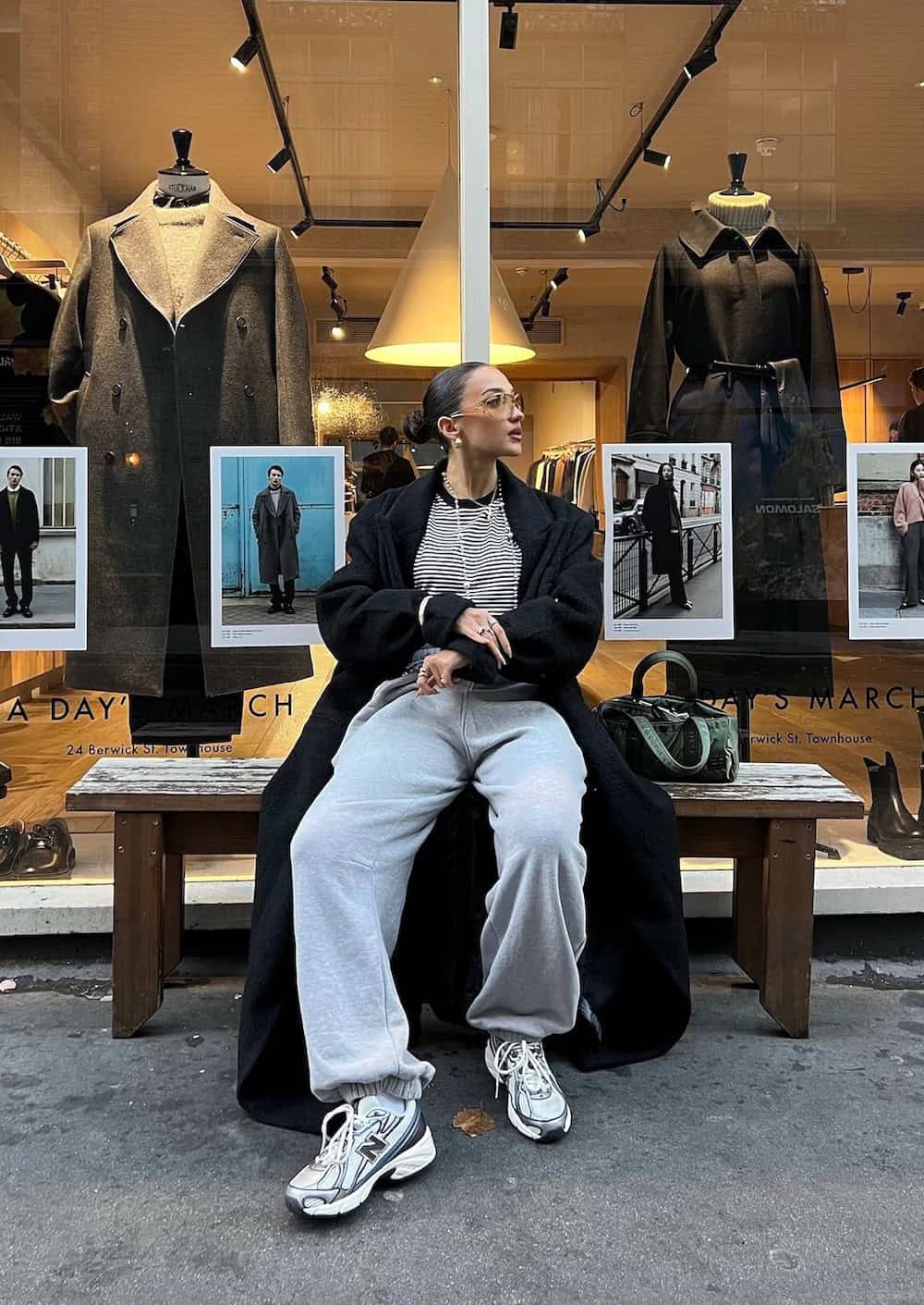 Woman wearing sweat pants with a striped tee and long coat with New Balance sneakers.