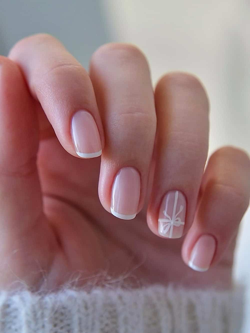 Short nude nails with white tips and a statement nail wrapped as a gift